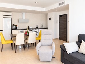 Una sala de estar moderna con un sillón gris, un sofá negro con almohadas blancas y un comedor con mesa y sillas.