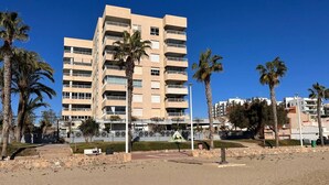 Un immeuble à plusieurs étages, doté de balcons, de palmiers et surplombant un ciel dégagé.