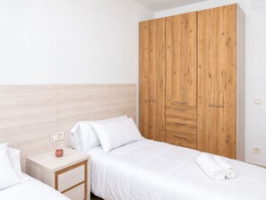 Quarto de hotel com duas camas, guarda-roupa de madeira, mesas de cabeceira e um criado-mudo.