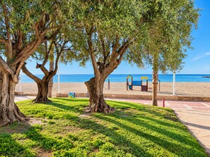 Un parque con árboles grandes, un área de juegos y una playa al fondo.