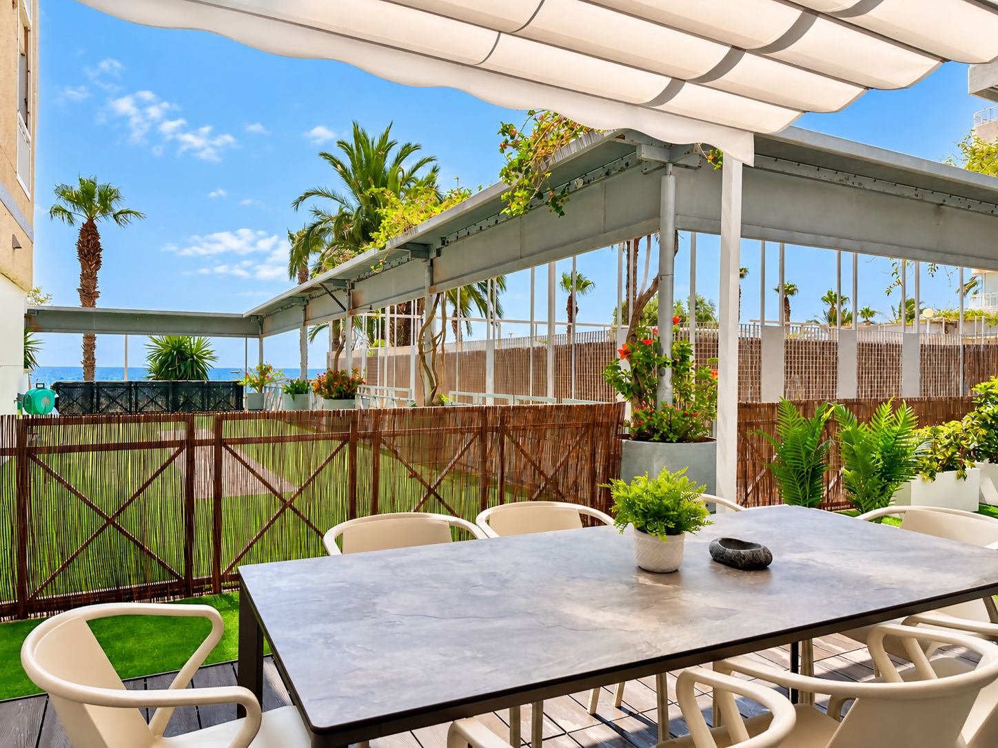 Une terrasse extérieure avec une table et des chaises, entourée de plantes et offrant une vue sur l’océan.