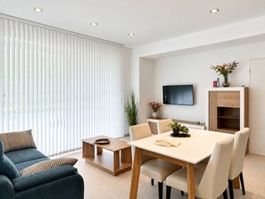 A modern living room with a sofa, a dining table, and a TV mounted on the wall. - Home 65E - Oceanfront with Private Terrace (Aguilas)