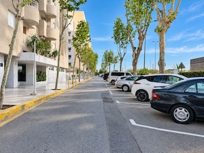 A street lined with parked cars and trees, with a building featuring balconies and a clear sky. - Home 65E - Oceanfront with Private Terrace (Aguilas)