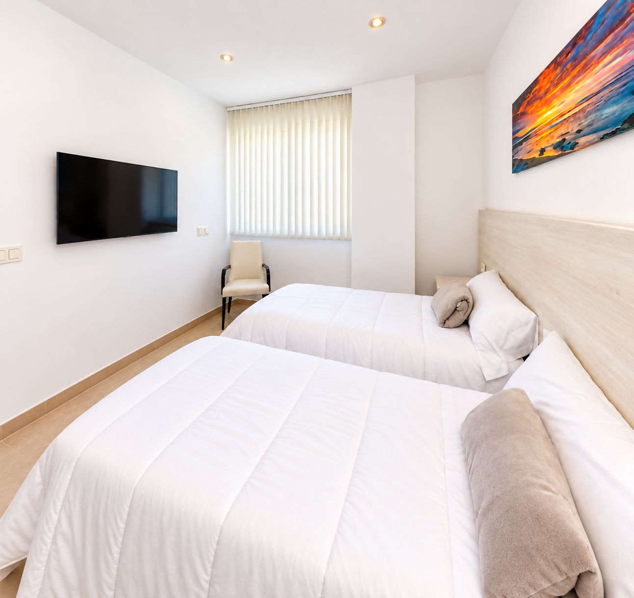 Ein Hotelzimmer mit zwei Betten, einem Fernseher, einem Sessel und einem Bild an der Wand.