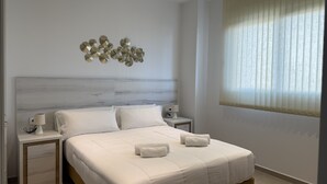 A bedroom with a bed, two bedside tables, a wall-mounted light fixture, and a window with curtains. - Home 65F - Beachfront with Private Terrace (Aguilas)