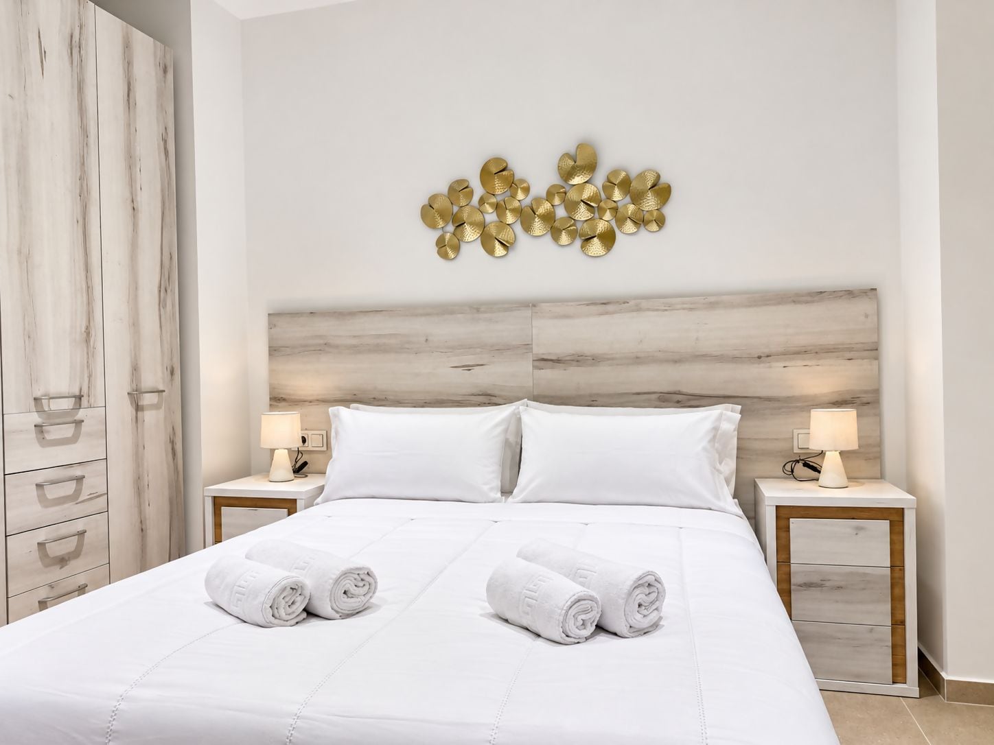 A hotel room with a bed, two bedside tables, a wardrobe, and a wall decoration.