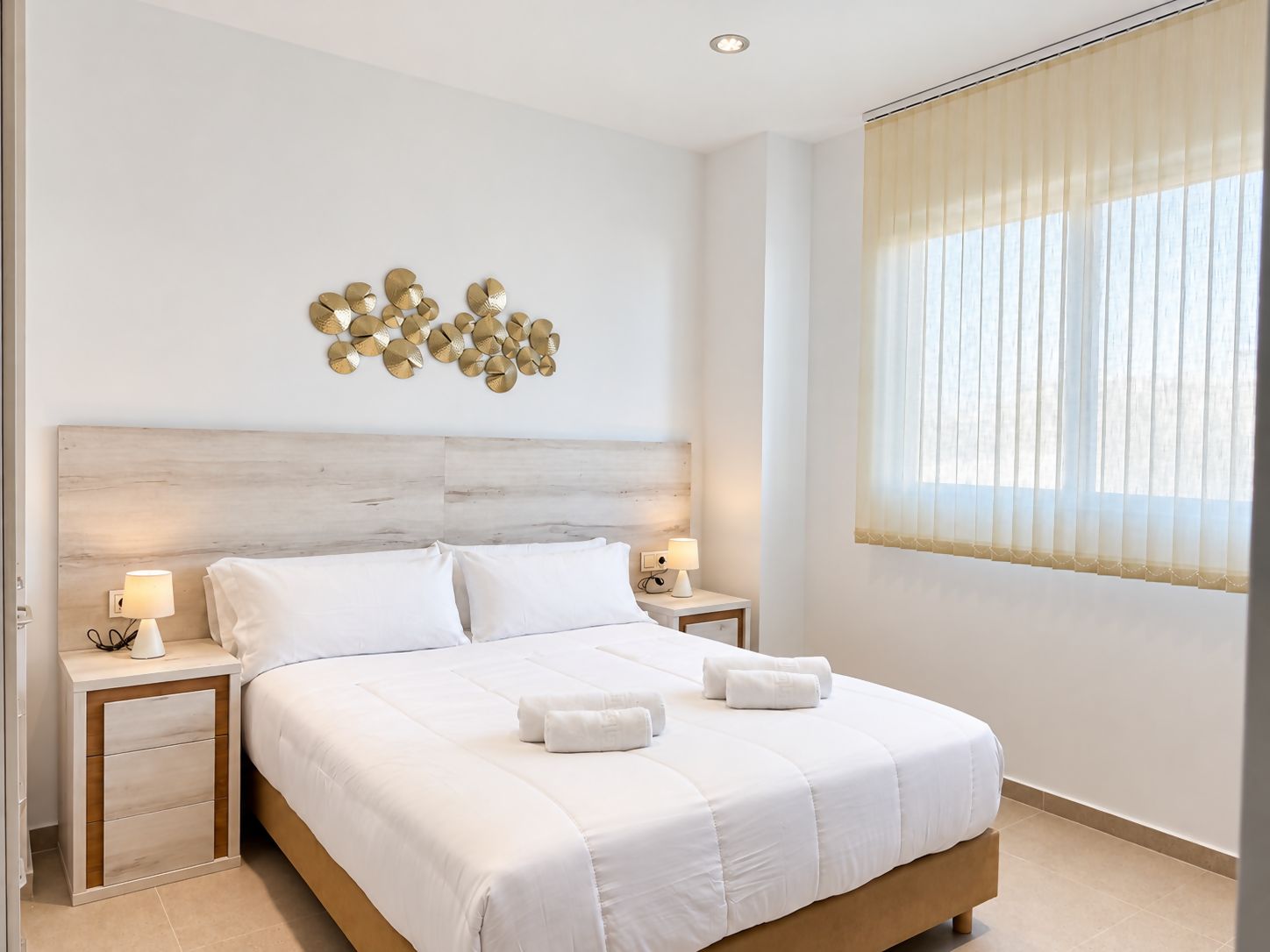 A hotel room with a large bed, two bedside tables, a decorative wall piece, and a window with curtains.