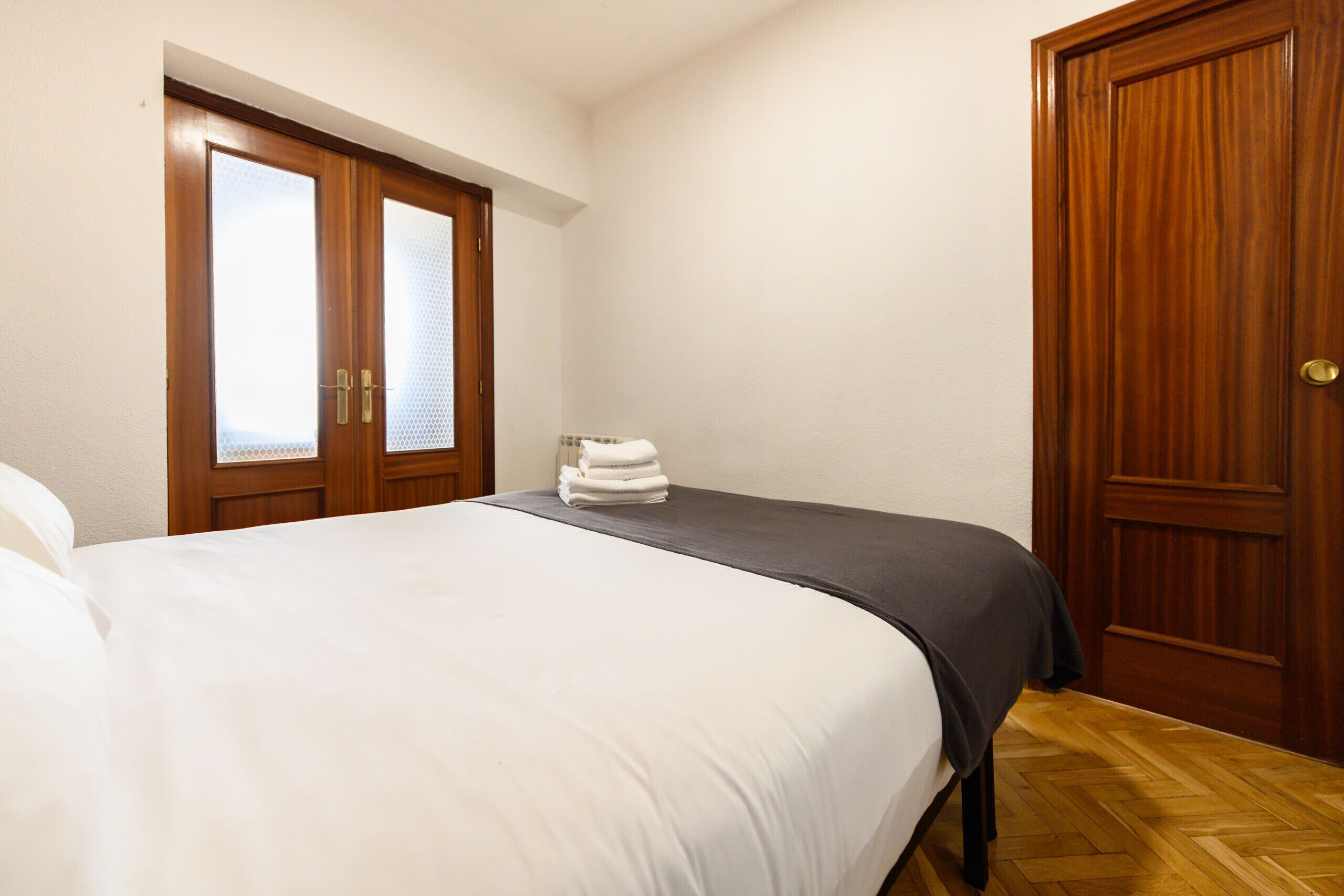 A bedroom with a bed, a wooden wardrobe, and a door with a window.
