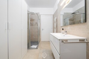 Ein modernes Badezimmer mit Duschkabine aus Glas, einem weißen Waschbecken und einem großen Spiegel.