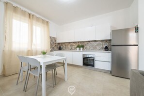 Eine moderne Küche mit weißen Schränken, einem Edelstahl-Kühlschrank und einer gefliesten Spritzschutzwand.