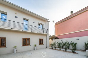 Ein zweistöckiges Gebäude mit Balkon, Blumentöpfen und einem kleinen Garten.