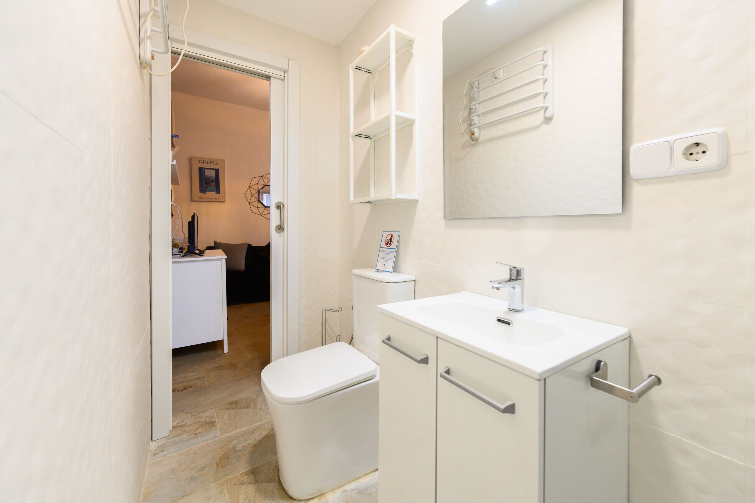 A modern bathroom with a white sink, toilet, and cabinet. There is a towel rack on the wall and a picture frame.