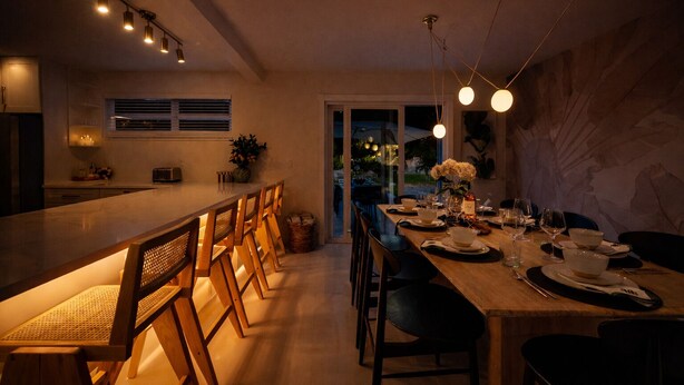 Een moderne keuken met een lange eettafel, houten stoelen en hanglampen.