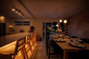 Uma cozinha moderna com uma mesa de jantar comprida, cadeiras de madeira e iluminação pendente.