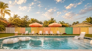 A swimming pool with lounge chairs and inflatable rings, surrounded by a colorful fence and palm trees. - Your Own Private Luxe Resort – 12 Mins to Beach! (West Palm Beach)