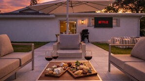 Een buitenruimte met een eettafel, een bord met Netflix erop, en een huis op de achtergrond.