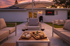An outdoor seating area with a table set for a meal, a sign for Netflix, and a house in the background. - Your Own Private Luxe Resort – 12 Mins to Beach! (West Palm Beach)