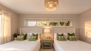 Een slaapkamer met twee bedden, een raam met uitzicht, een nachtkastje met lamp en een decoratieve plafondlamp.