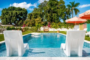 A swimming pool with two white lounge chairs facing the water, surrounded by lush greenery and a palm tree. - Your Own Private Luxe Resort – 12 Mins to Beach! (West Palm Beach)