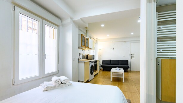 Een hotelkamer met een bed, een kleine kitchenette, een wasmachine, een bank en een houten vloer.