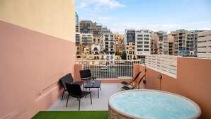 Een terras op het dak met een jacuzzi, buiten zitplaatsen en een uitzicht op de stad.