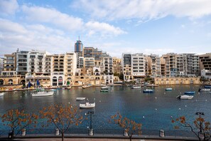 A waterfront view with multiple boats docked, a variety of buildings including a prominent tower, and a clear sky. - Sumptuous townhouse, sea view roof terrace GOSTJ-2 (St Julian's)