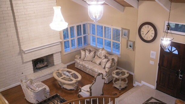 A spacious living room with a fireplace, a sofa, and a coffee table. There are two hanging light fixtures and a clock on the wall.