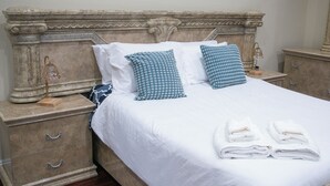 A neatly made bed with white linens and two blue patterned pillows, a bedside lamp, and a wooden nightstand with drawers.