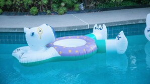 An inflatable pool float shaped like a bear with a purple and white polka dot ring.
