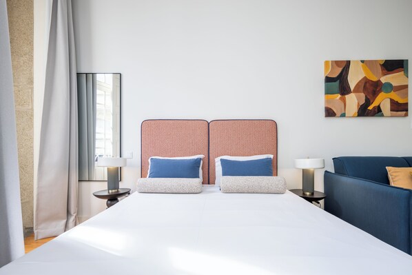 Une chambre d’hôtel avec un grand lit, deux tables de chevet avec des lampes, un canapé bleu et un tableau au mur.