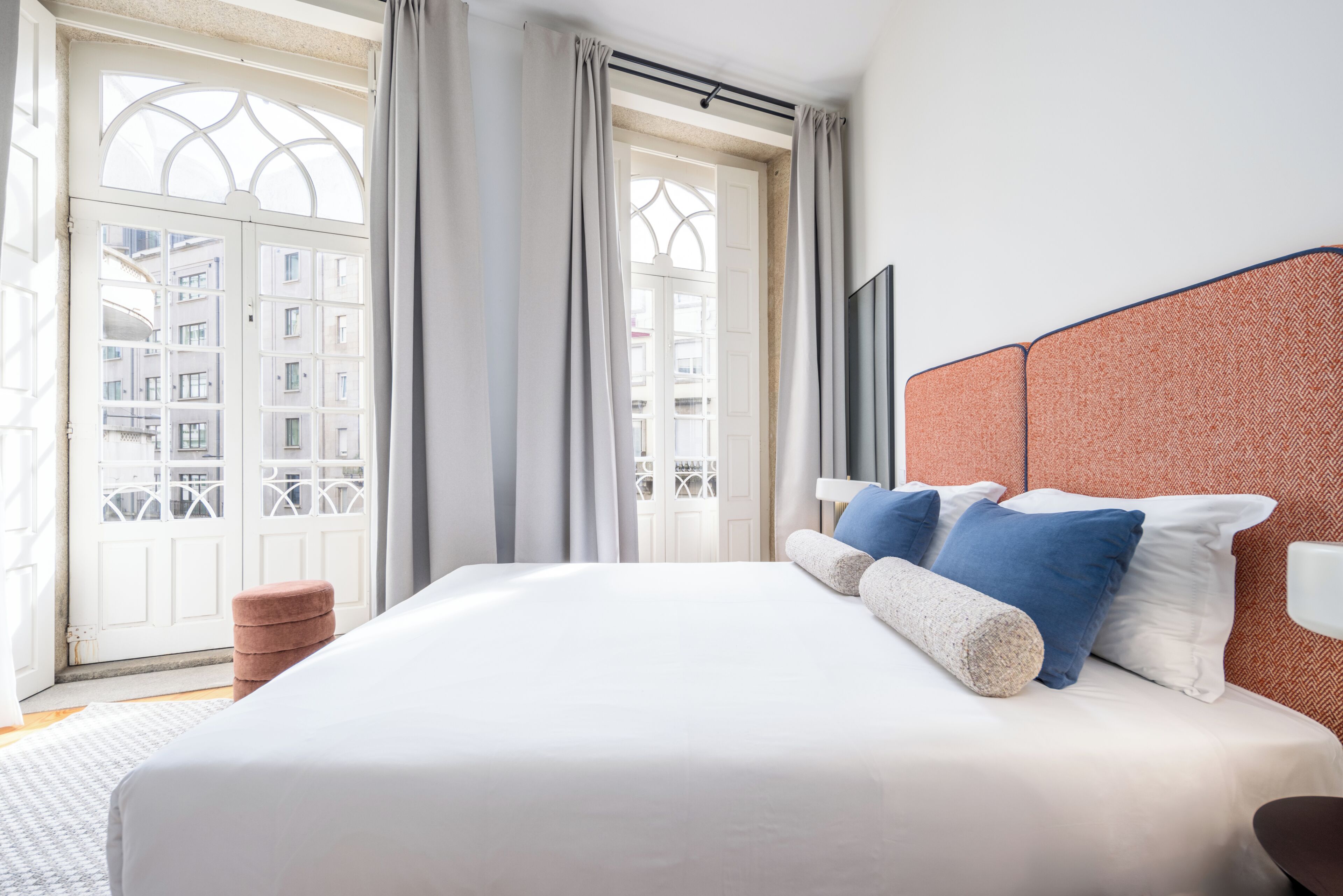 Ein Hotelzimmer mit einem großen Bett, Blick auf ein Gebäude durch eine Glastür und einem Balkon.