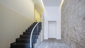 Un escalier avec des marches noires et une rampe blanche, menant à une porte adossée à un mur de pierre.