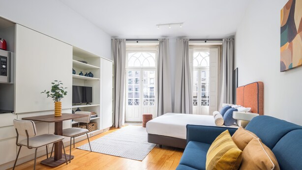 Une chambre d’hôtel moderne avec un lit, un canapé bleu, un bureau avec une chaise, une télévision et une grande fenêtre avec des rideaux.