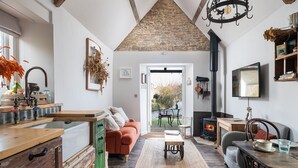 A cozy living room with a fireplace, a kitchen area with wooden cabinets, and a dining area with a table and chairs. - Filly Island - sleeps 2 guests  in 1 bedroom (South Cerney)