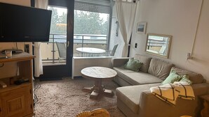 A cozy living room with a sofa, a small round table, a television, and a balcony with a view of trees. - Complete Winterberg residence Fichtenweg 54, near the slopes and Bikepark. (Winterberg)