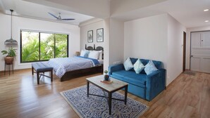 A spacious room with a large bed, a blue sofa, a small table, and a window with a view of greenery. - 7 BHK villa with Private pool near Siolim and Anjuna (Siolim)