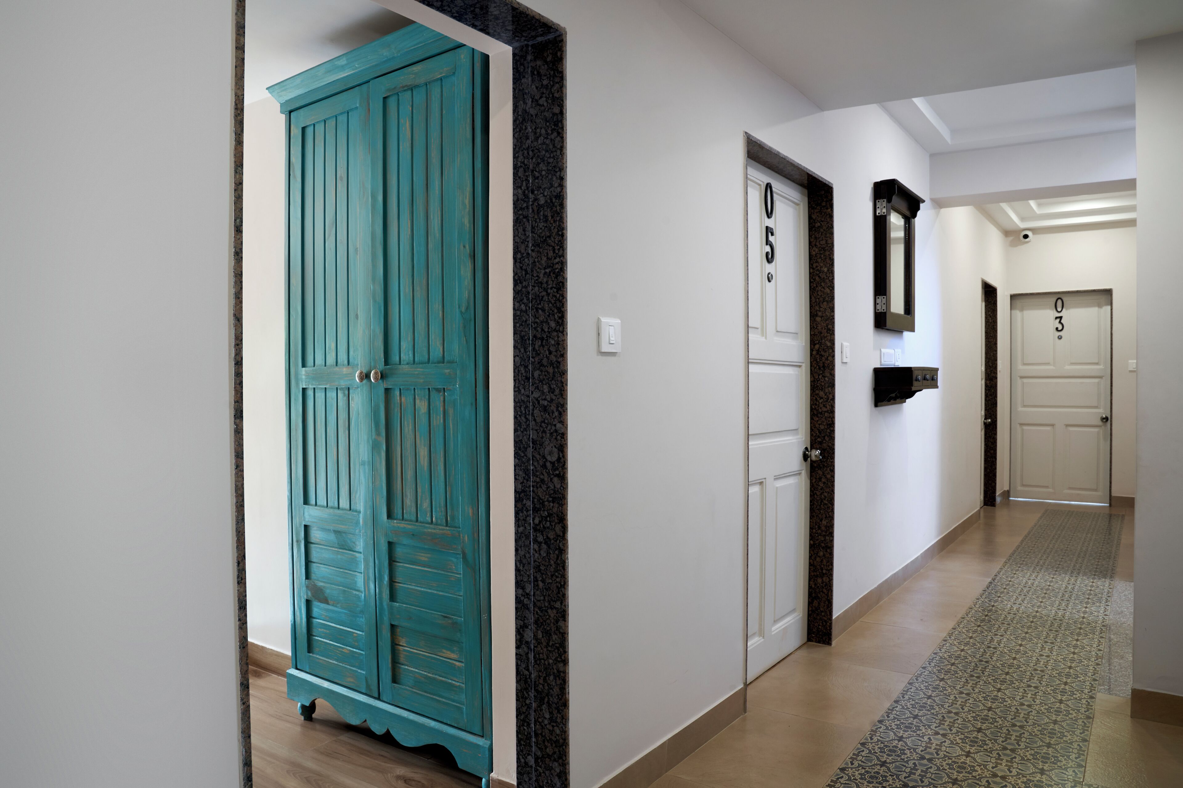 A hallway with a teal door labeled '05', a white door labeled '03', and a mirror on the wall.