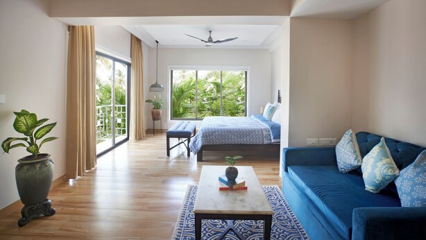 A spacious room with a large bed, a blue sofa, a small table with a plant, and a view of greenery through a large window. - 7 BHK villa with Private pool near Siolim and Anjuna (Siolim)