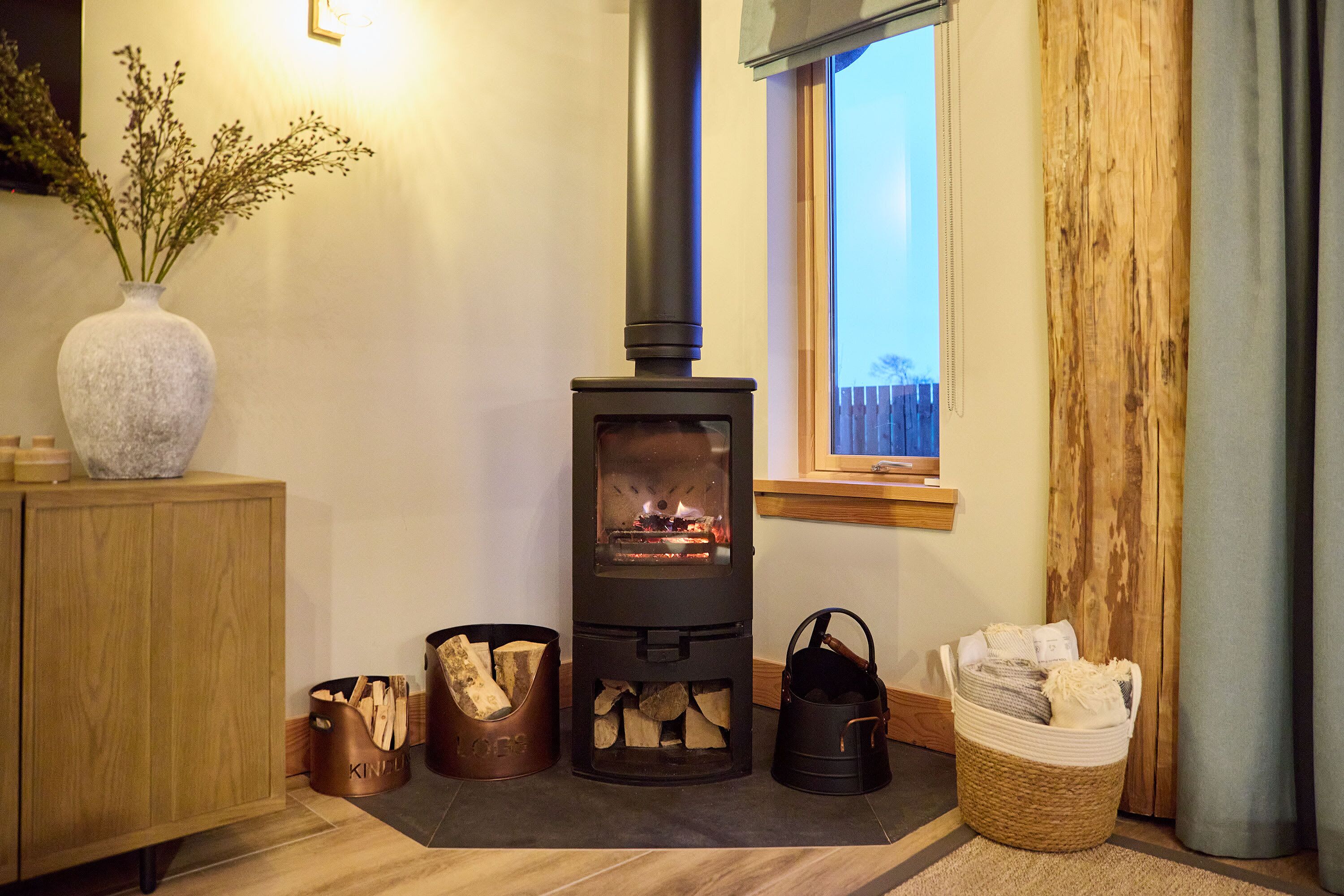 A cozy room with a wood-burning stove, a wooden cabinet, and a vase with flowers.