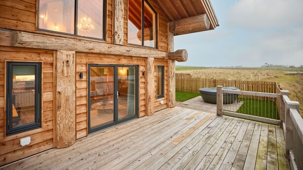 Eine Holzhütte mit großen Fenstern, einer Terrasse und Blick auf die Landschaft.