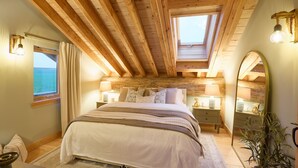 Ein Schlafzimmer mit einem großen Bett, Holzbalken, einem Oberlicht, einem Nachttisch mit Lampe, einem Spiegel und Meerblick.