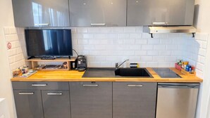 A modern kitchen with grey cabinets, a black countertop, a built-in stove, a sink, and a dishwasher. - Studio - marina sea view- smart (Villeneuve-Loubet)