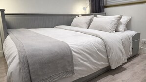 A neatly made bed with a grey blanket and white bedding in a modern room with a grey headboard and a bedside table. - Studio - marina sea view- smart (Villeneuve-Loubet)