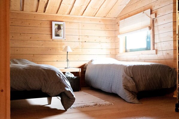 A wooden cabin room with two beds, a nightstand, a lamp, and a window.