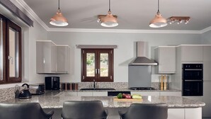 Uma cozinha moderna com ilha central, banquetas, bancadas de granito, eletrodomésticos de aço inoxidável e iluminação pendente.