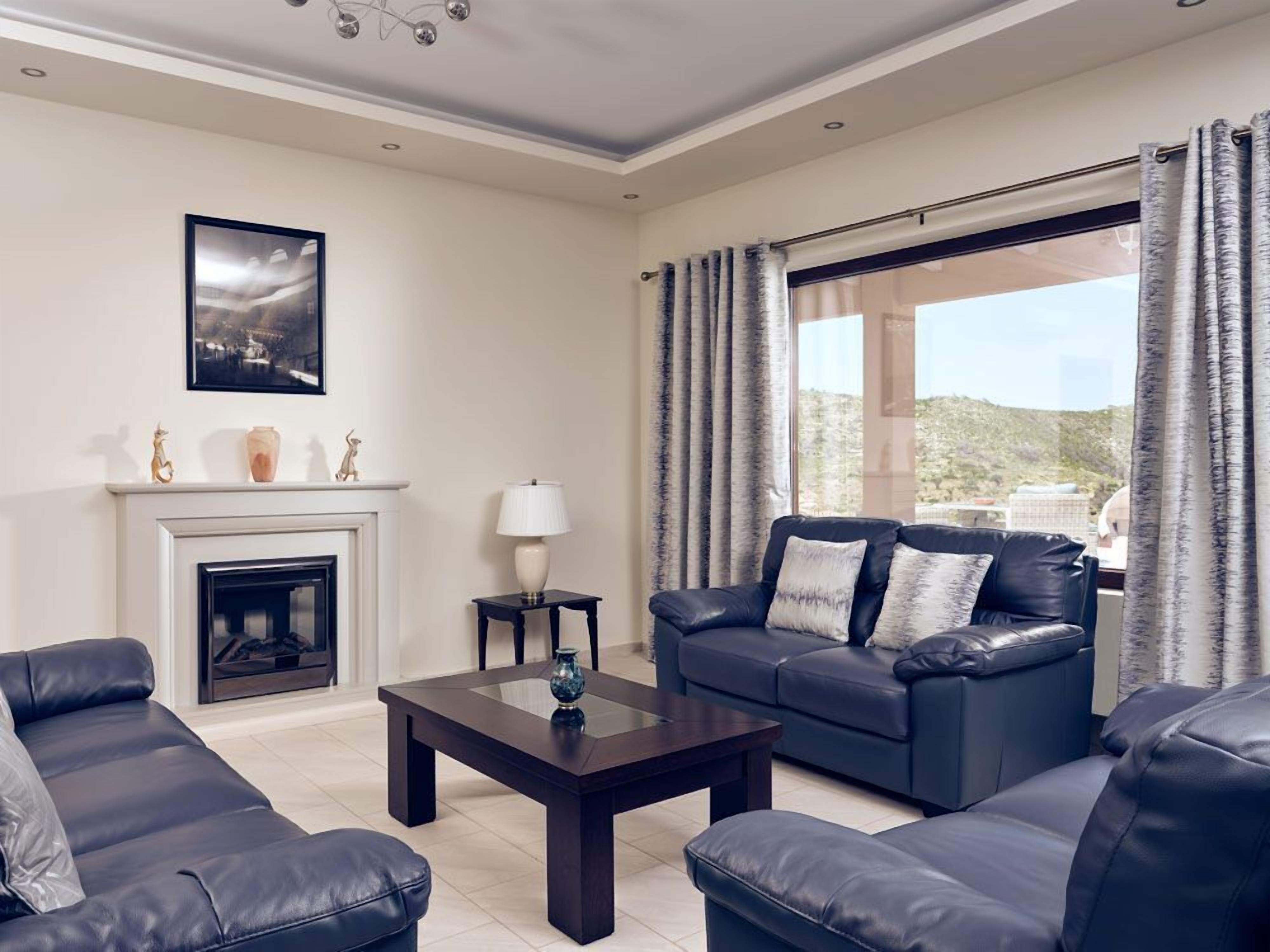 A living room with a fireplace, a sofa set, a coffee table, and a large window with curtains.