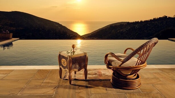 Uma cadeira de vime e uma mesa pequena perto de uma piscina com vista para o pôr do sol.