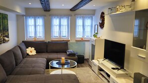 Una sala de estar moderna con un sofá modular, un televisor de pantalla plana y un cuadro de un arroyo en el bosque.