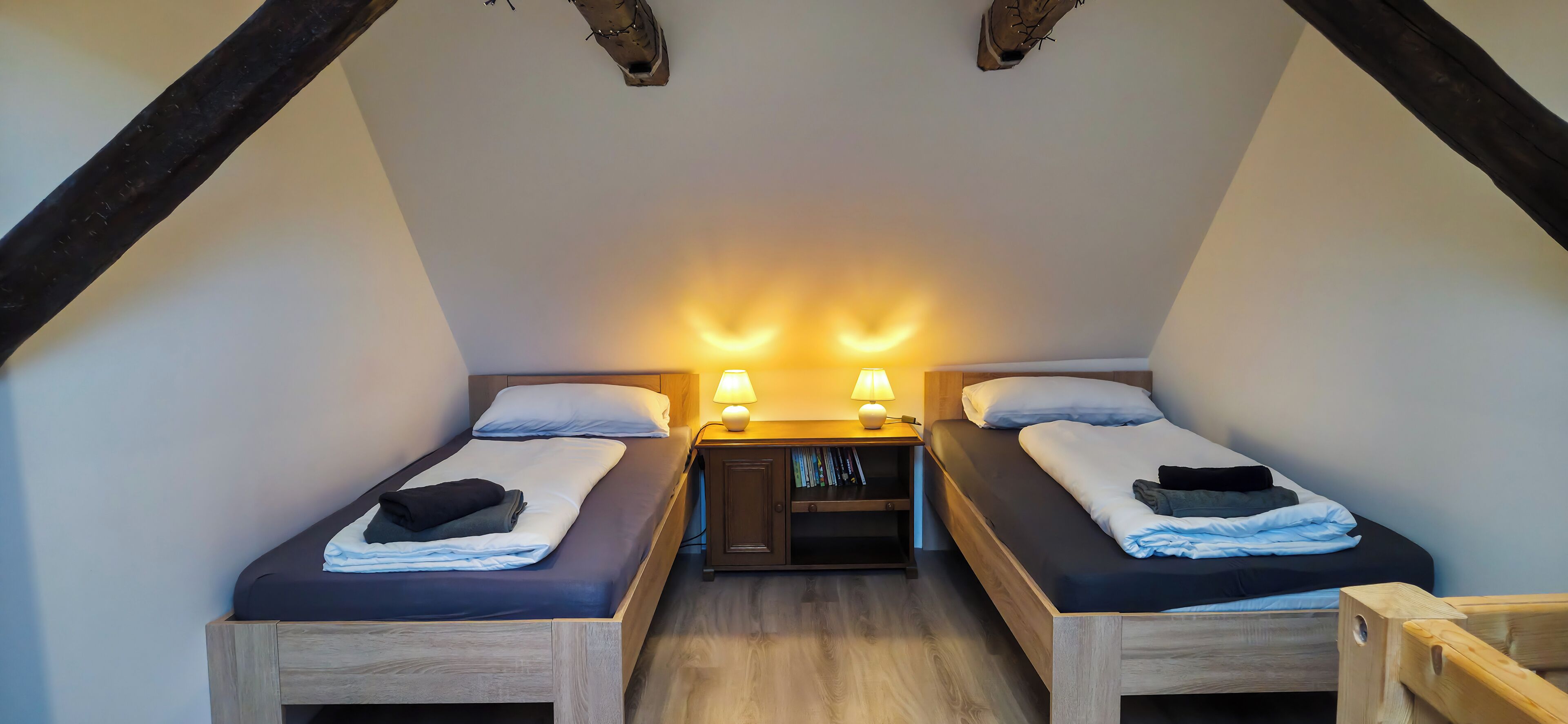 Un dormitorio pequeño y acogedor con dos camas individuales, cabeceras de madera y una mesita de noche con una lámpara entre ellas.