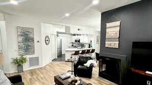 A modern living room with a dark sofa, a coffee table with decorative items, a TV, and a fireplace. - Modern Resort Escape (Tempe)